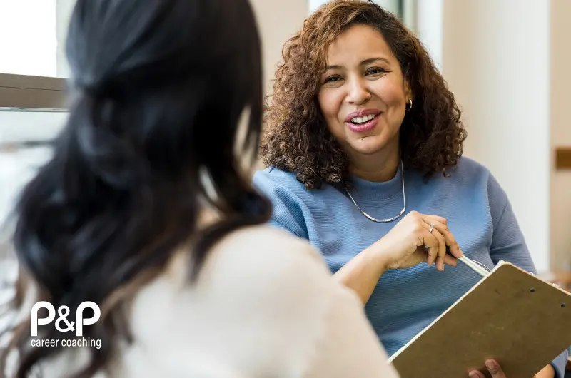 Two women having a conversation, the women facing is holding a clipboard and pointing at the content with a pen